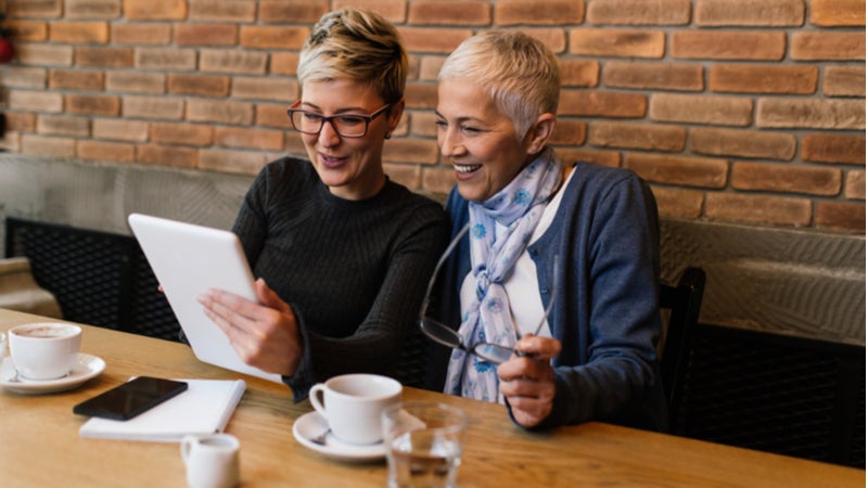 Woman and her older mother look together at tablet in cafe