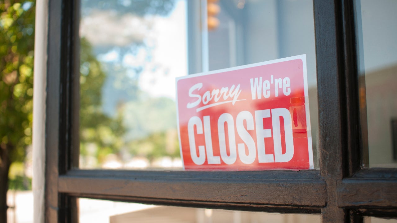 A Sorry we're closed sign hands in a shop window