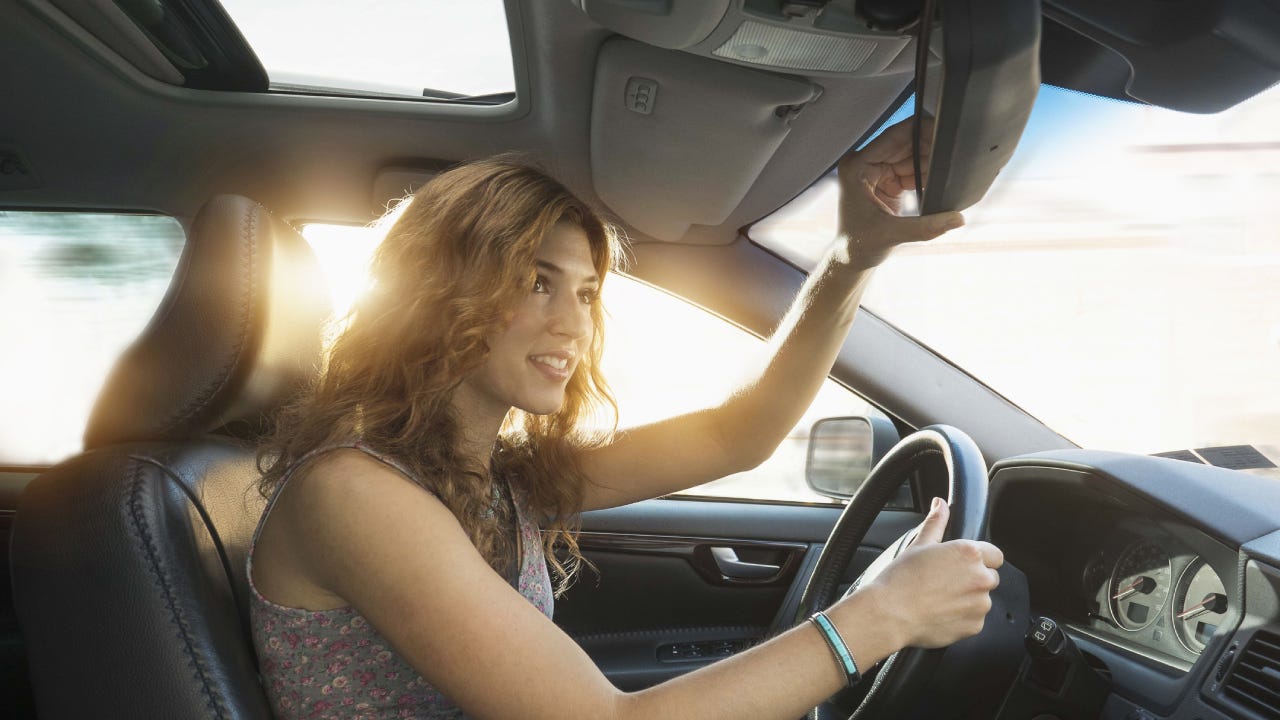 A woman adjusts her rearview mirror before she gets ready to drive away.