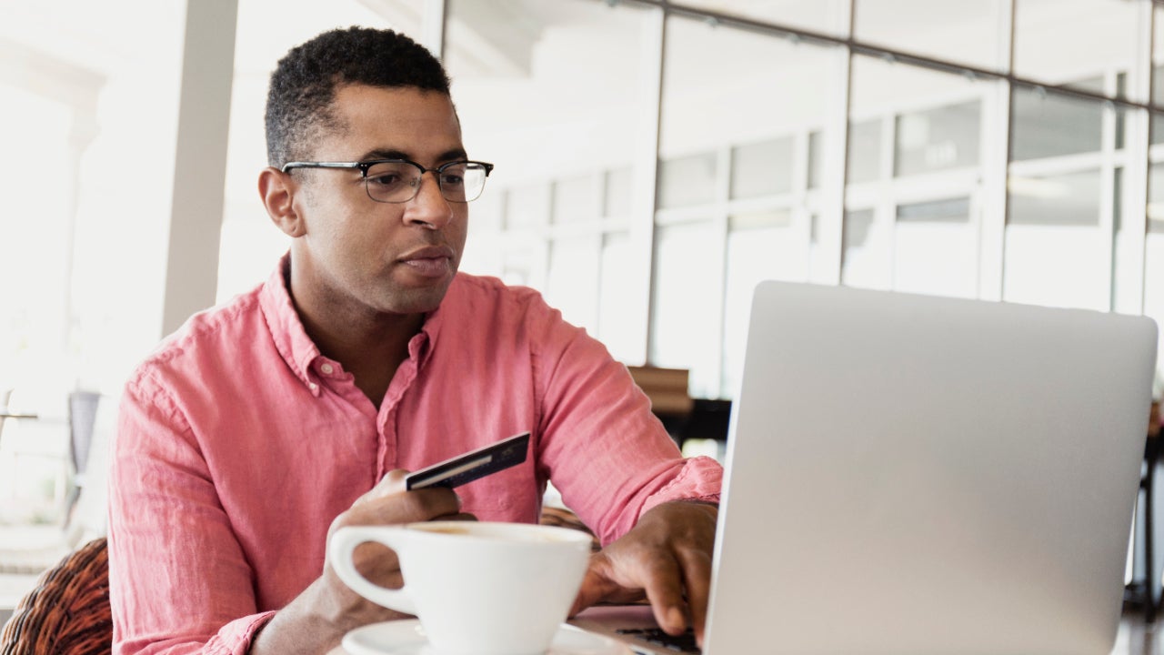 Man in coffee shop using laptop with a card in his hand.