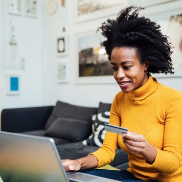 Young woman uses credit card snd laptop in living room