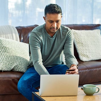 man sitting on the couch while working on laptop and holding credit card