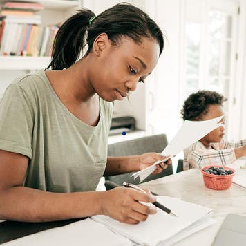 Mom preparing financial paperwork at home while her child draws next to her