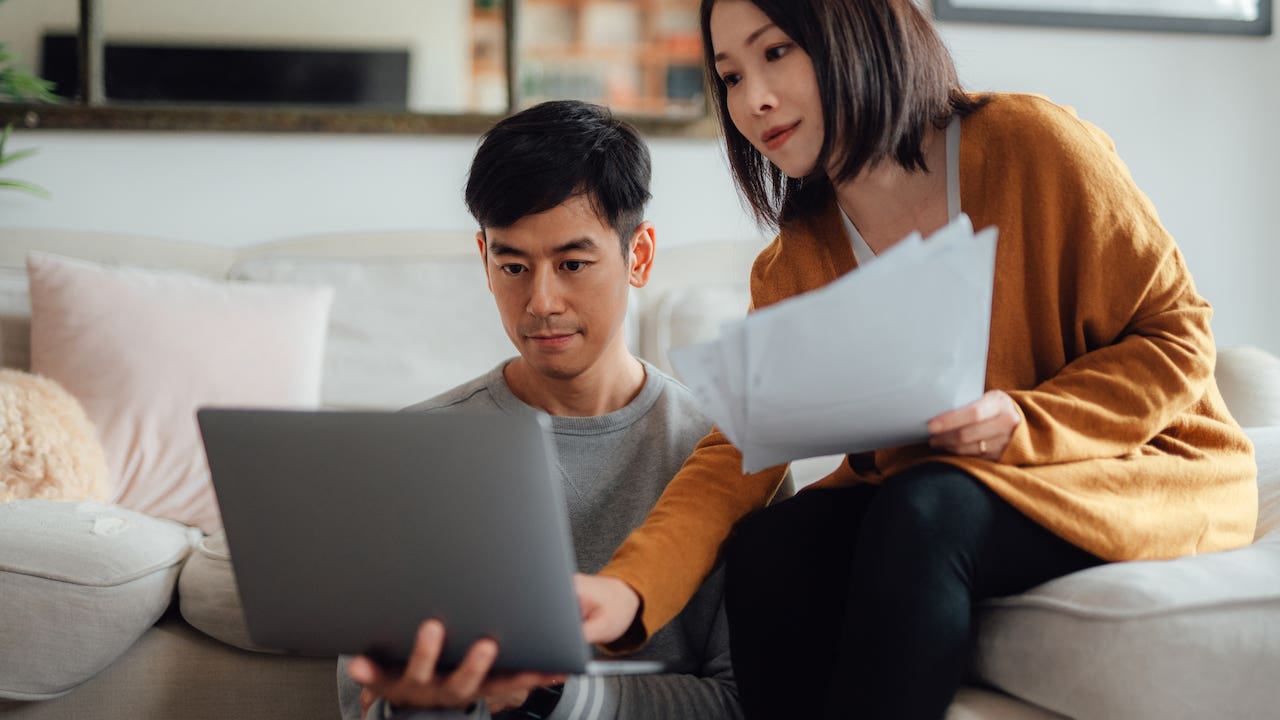 Serious looking young couple discussing over financial bills while using laptop in living room.