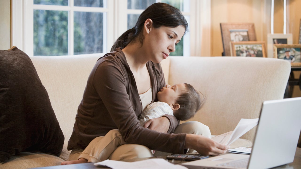 Hispanic woman paying bills online with sleeping baby