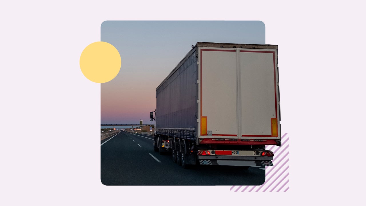 The back of a semi truck driving on a highway during sunset.