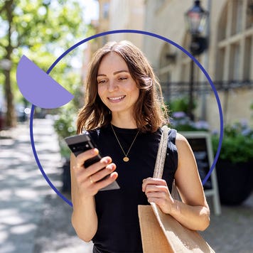 Young woman smiling and walking down a city street with here cellphone out