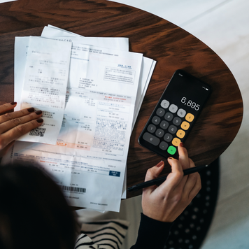 Overhead view of young Asian woman managing personal banking and finance at home. Planning budget and calculating expenses while checking her bills with calculator. Managing taxes and financial bills. Home budgeting. Concept of finance and economy