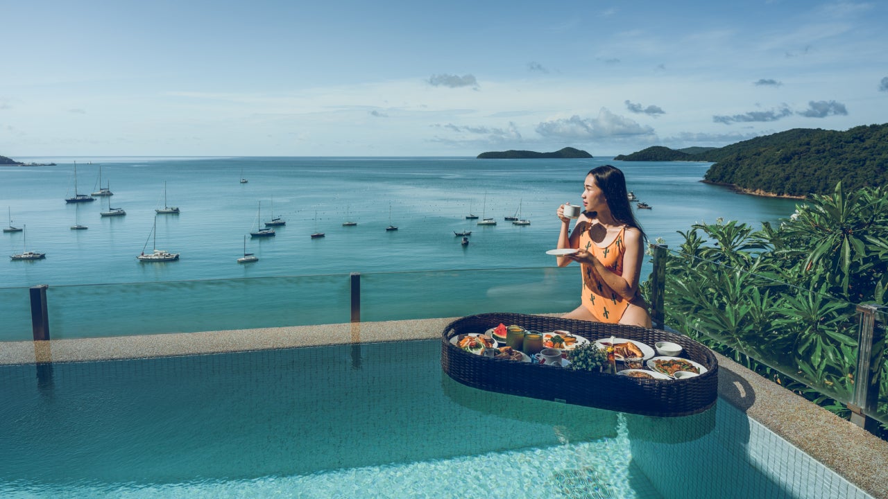 A woman drinking coffee and breakfast floating on the water beside the pool.