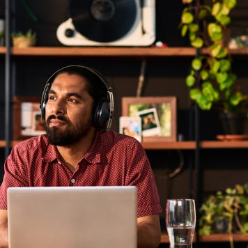 Mid adult man wearing headphones using laptop and looking away