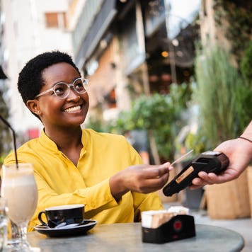 Young African American woman woman sitting at the cafe and paying for her coffee with a credit card