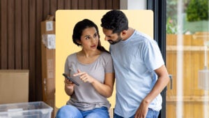 A woman and man standing close to each other while discussing what they see on their mobile phone.
