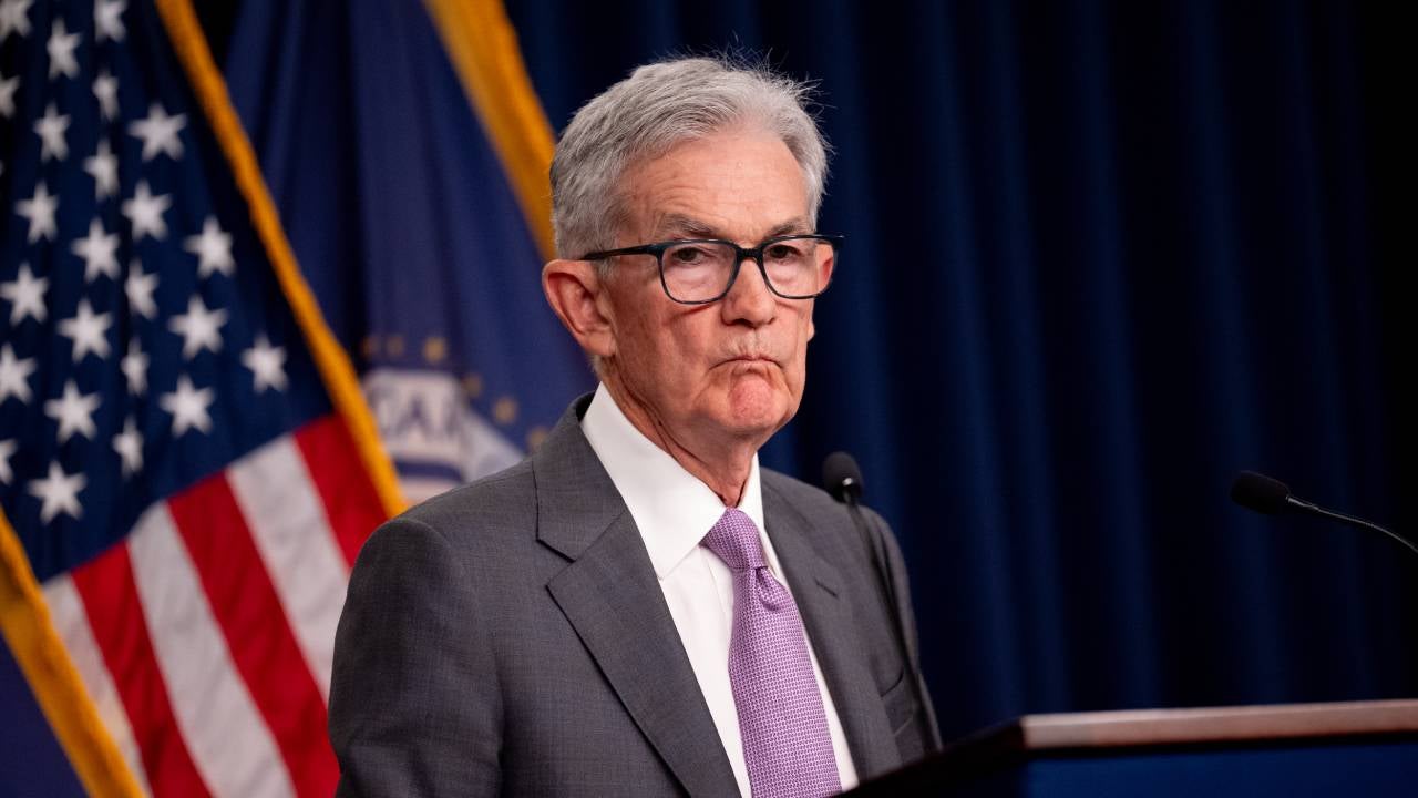 Federal Reserve Chair Jerome Powell standing at a lectern with an American flag in the background.
