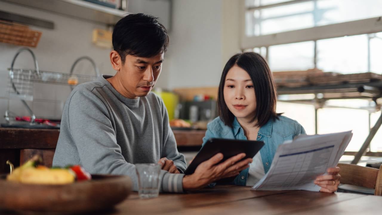 An Asian couple planning finances with a digital tablet at home.