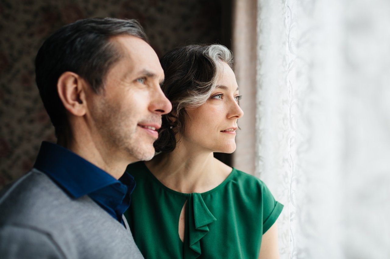 A mature couple is looking out of a bright window.