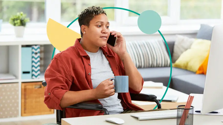 Person sitting at a desk, holding a mug in their right hand, and talking on their mobile phone.