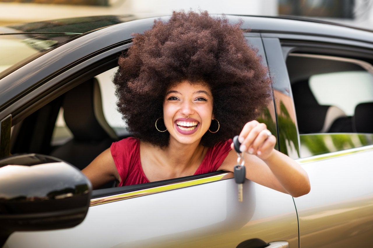 Smiling young woman showing car key while sitting in car