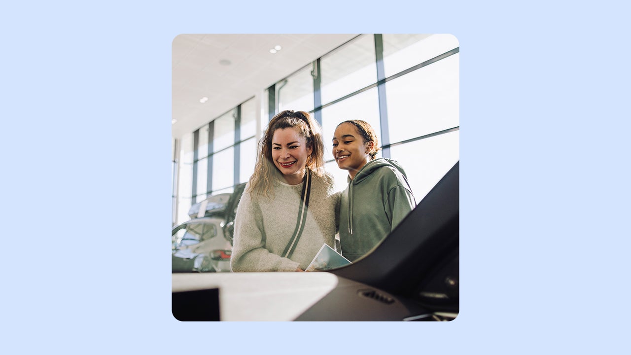 A smiling woman and her daughter look in at a car. There is an illustrated blue background.