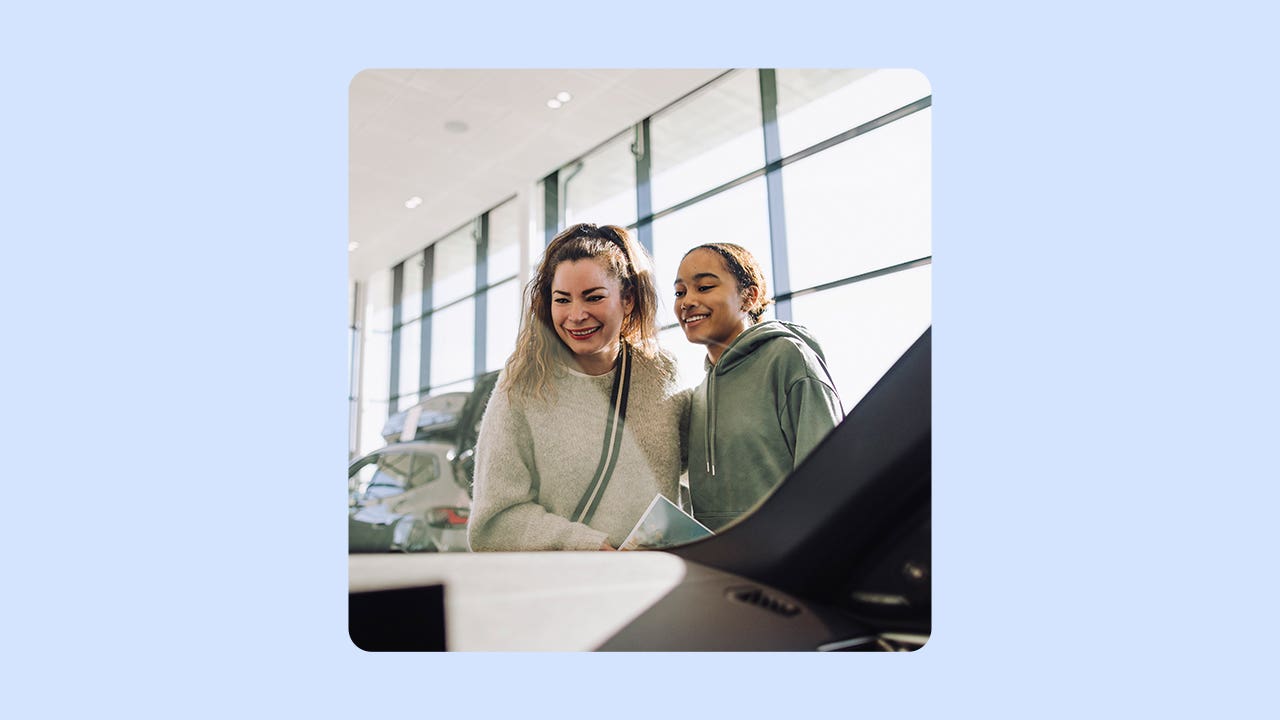 A smiling woman and her daughter look in at a car. There is an illustrated blue background.