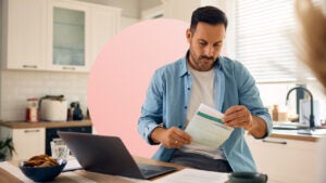 design image of a man looking at a piece of paper while on his laptop