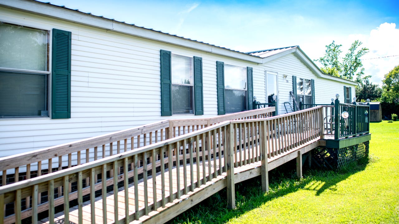 The side of a mobile home with a wheelchair ramp leading to the front door