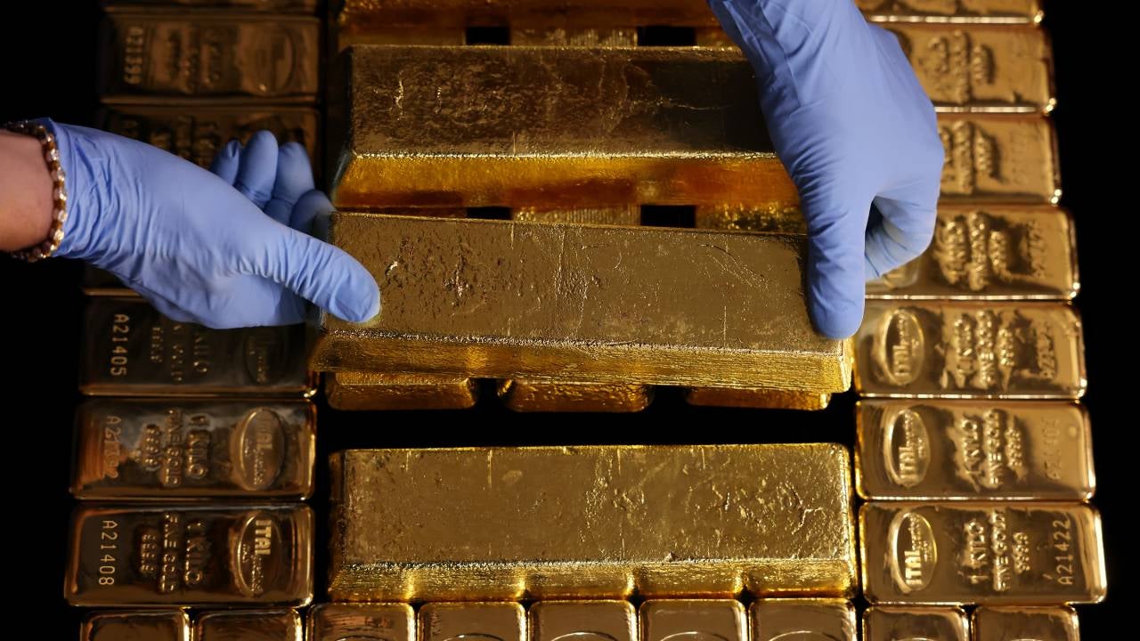 Pair of gloved hands lifting a gold bar.