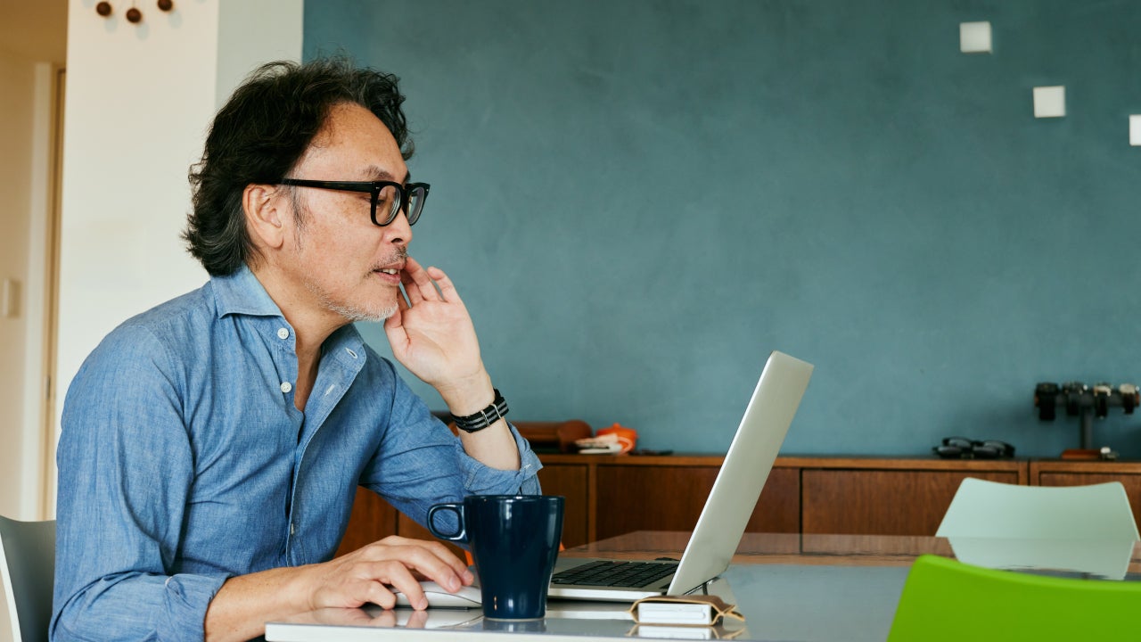 An older man looks at his investments on a laptop.