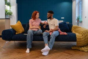 Man and woman sit on a couch with serious expressions.