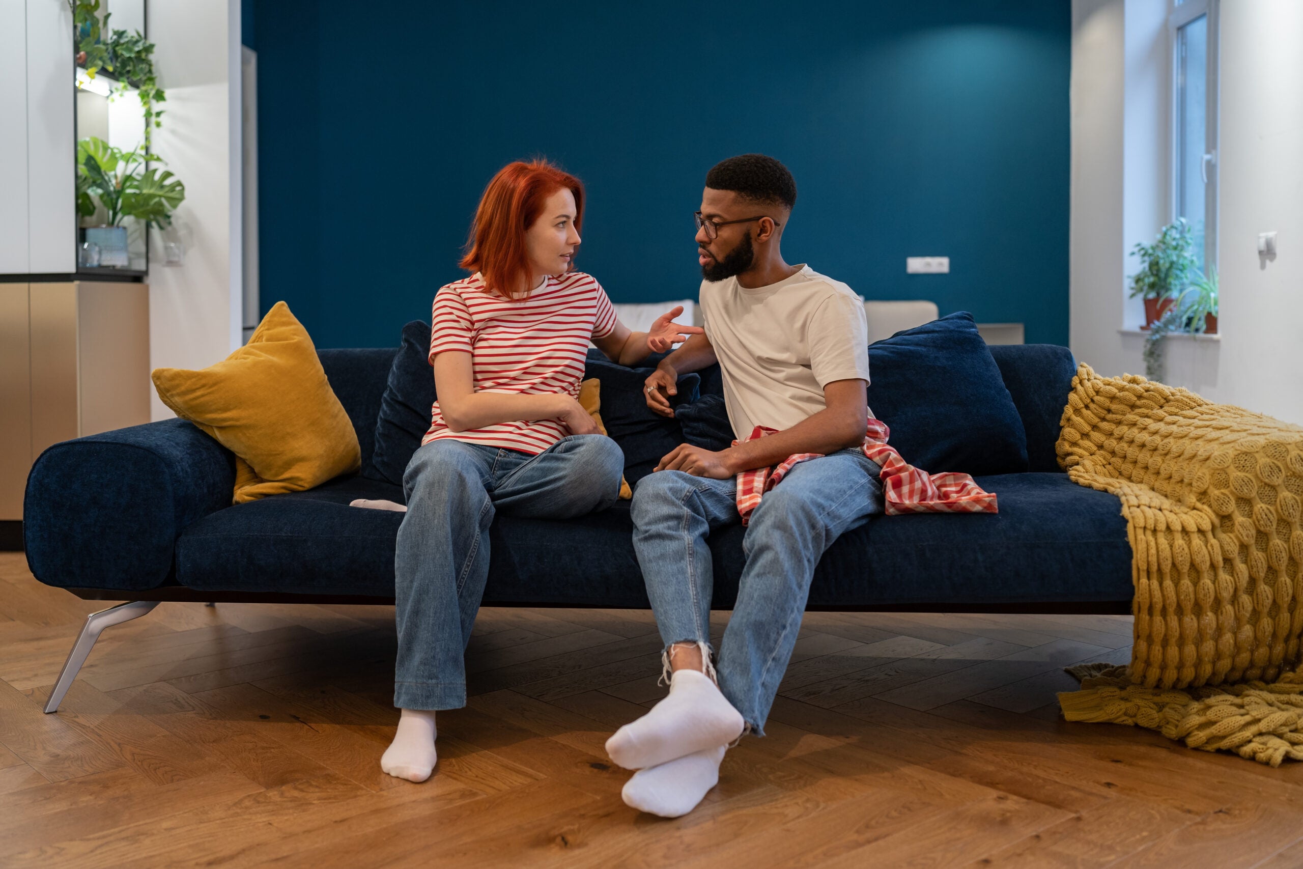 Man and woman sit on a couch with serious expressions.