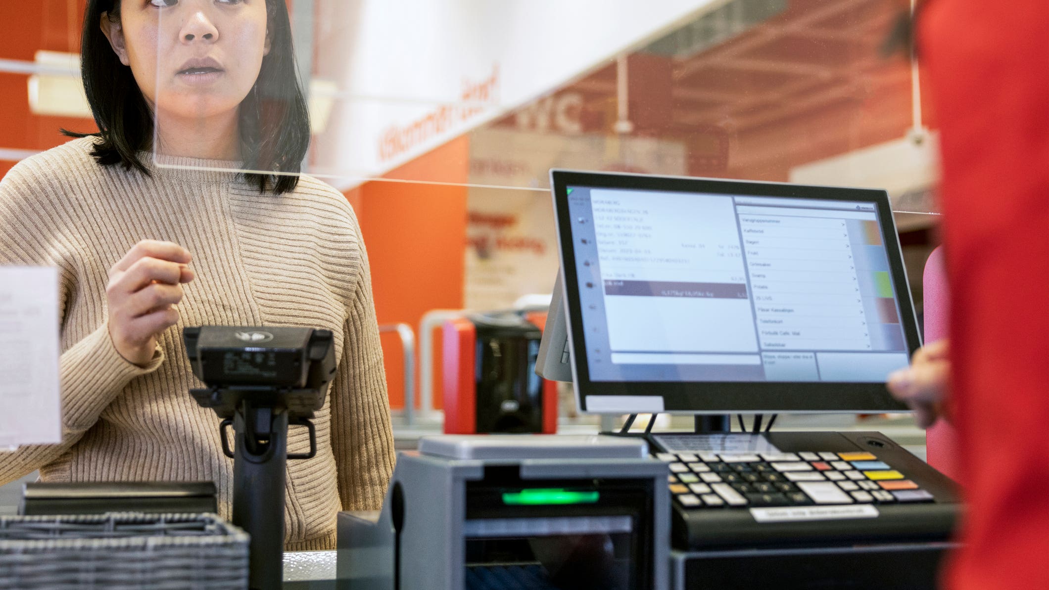 Young female customer talking to cashier at checkout in supermarket