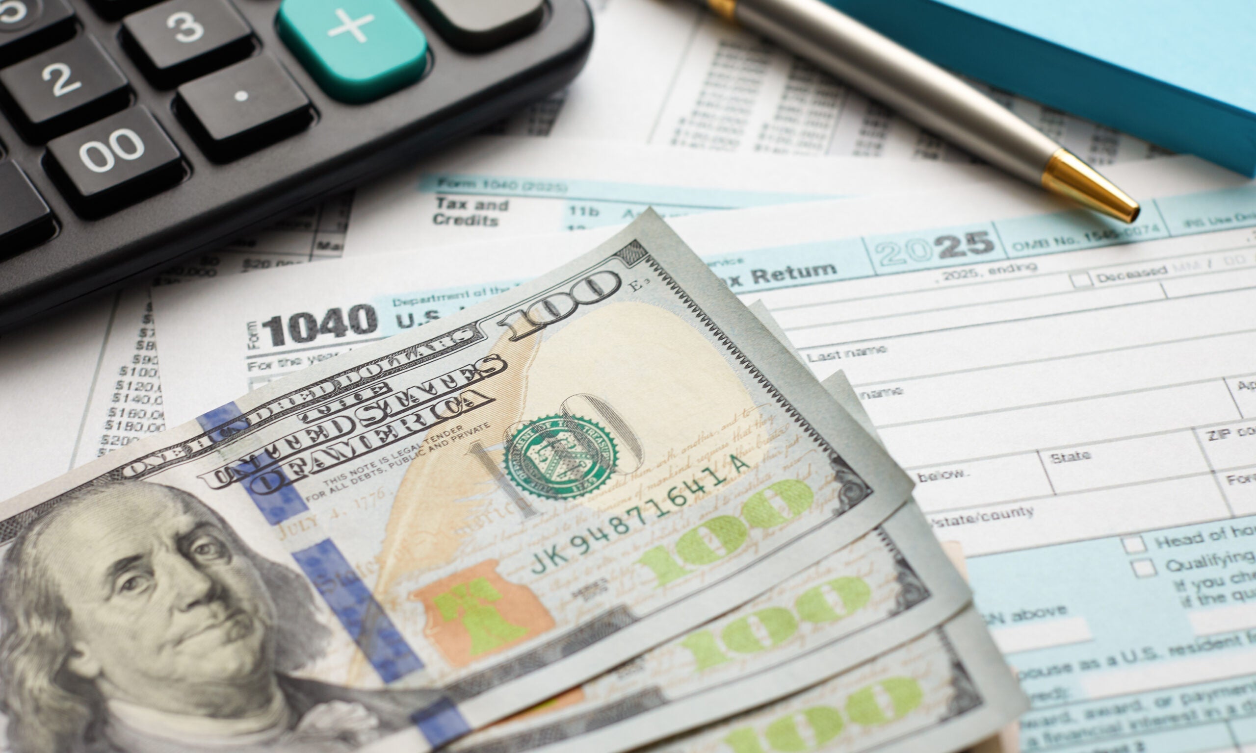 $100 bills lay on top of a 1040 U.S. Federal tax form.